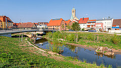 Brücke über einem Fluss mit grünem Ufer vor einer Stadt