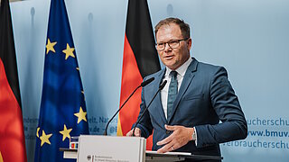 Carsten Schneider am Rednerpult mit Deutschland- und EU-Flagge im Hintergrund