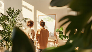 Zwei Frauen besprechen sich vor einer Stellwand