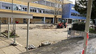 Innenhof eines Schulgebäudes mit aufgerissenem Boden und kleinem Traktor