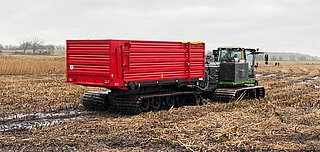 Große landwirtschaftliche Raupenmaschine mit rotem Anhänger auf feuchtem, abgeerntetem Feld