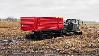 Große landwirtschaftliche Raupenmaschine mit rotem Anhänger auf feuchtem, abgeerntetem Feld
