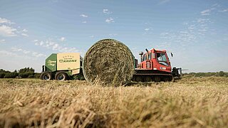 Raupe zieht landwirtschaftliche Maschine, die großen runden Heuballen auf Feld presst