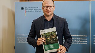 Bundesumweltminister Carsten Schneider hält die Vorschläge zur Weiterentwicklung des Aktionsprogramms Natürlicher Klimaschutzin der Hand.