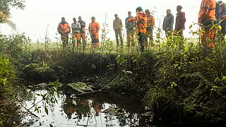Eine Gruppe von Menschen steht an einem renaturierten Bach