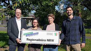 Vier Personen halten ein Schild mit der Aufschrift Regionalbüro NRW