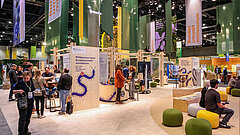 Messestand mit Bannern des Bundesumweltministeriums auf einer Messe mit mehreren Besuchern und Sitzgelegenheiten