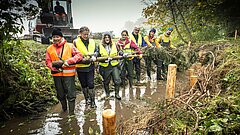 Mehrere Personen stehen in einem kleinen Fluss und entfernen einen Baumstamm.