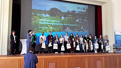Die Moorspezialist*innen auf einer Bühne vor einer großen Leinwand