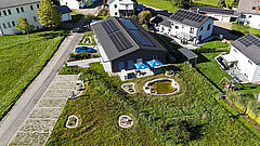 Luftaufnahme eines naturnah gestalteten Firmengeländes mit Solardach, Teich, Sitzbereich und vielfältigen Grünflächen.